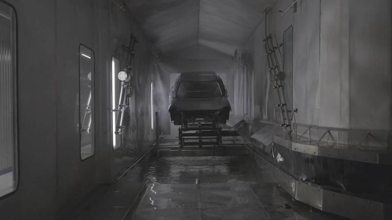 Unpainted body shell is lowered into a large pool of liquid, to be washed in preparation for painting.