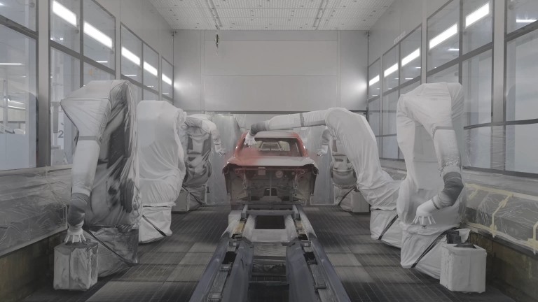 In the paint shop, robots in the process of applying a red body colour to the car shell.