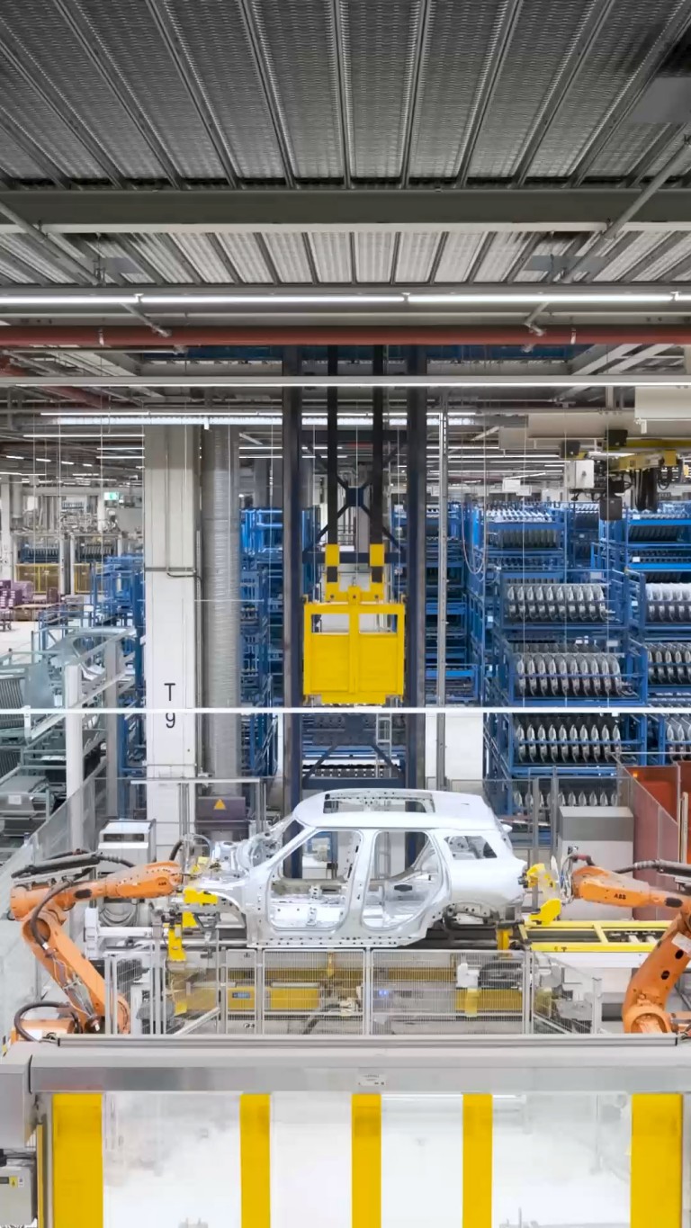 Side view of the MINI Countryman body shell as it is lifted high in the air by a bright yellow industrial cargo elevator.