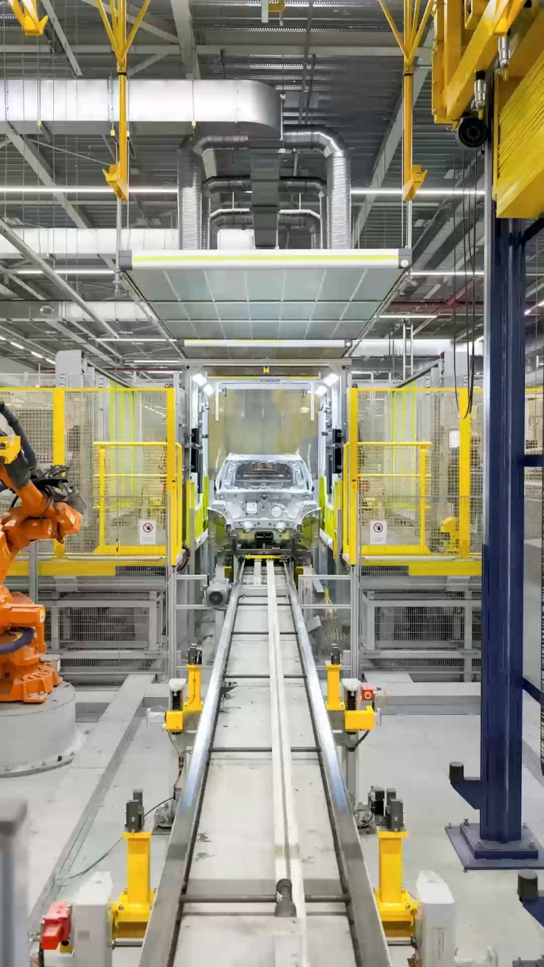 Zoomed-in viewpoint of the front-facing MINI Countryman body shell as it is secured and lifted by a bright yellow industrial elevator.